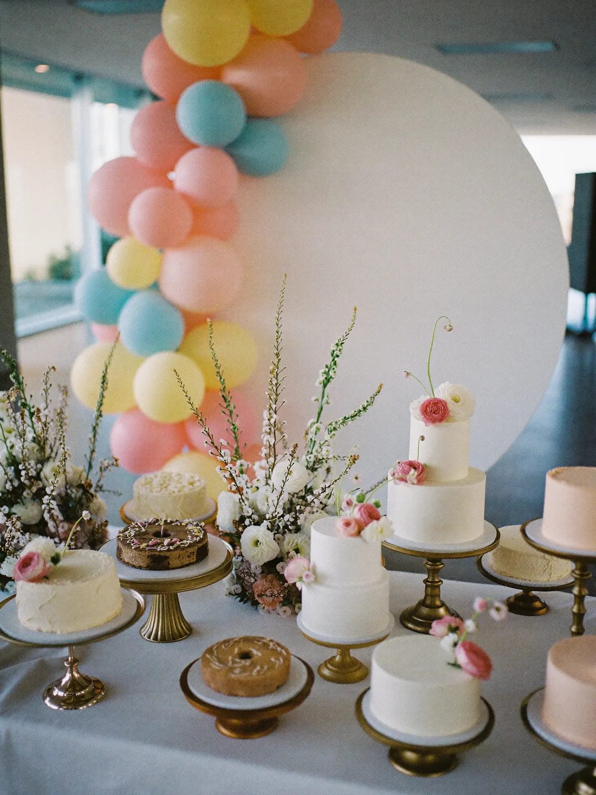 A dessert table with cakes, florals and a balloon garland
